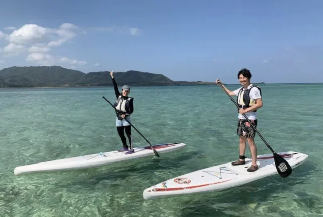 小浜島ランチの合間に、透き通るエメラルドグリーンの海でサップ（SUP）体験を満喫する観光客