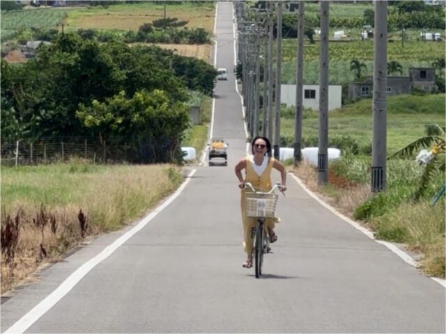 小浜島ランチの目的地へ向かって、のどかな一本道を爽快にサイクリングする女性